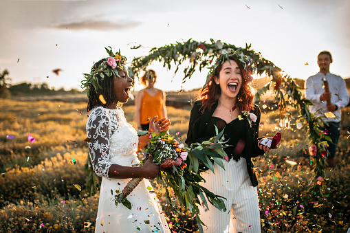 Lesbian wedding party. Two brides on wedding ceremony, surprised with confetti standing in a front of outdoor wedding arch